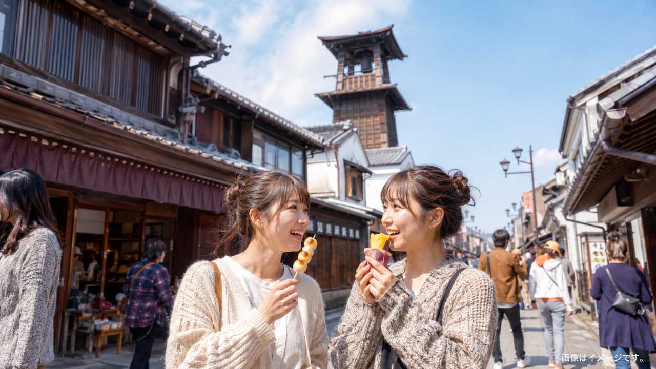 蔵造りの町並みと時の鐘を背景に、さつまいもスイーツや団子を手にした観光客の雰囲気を自然に表現