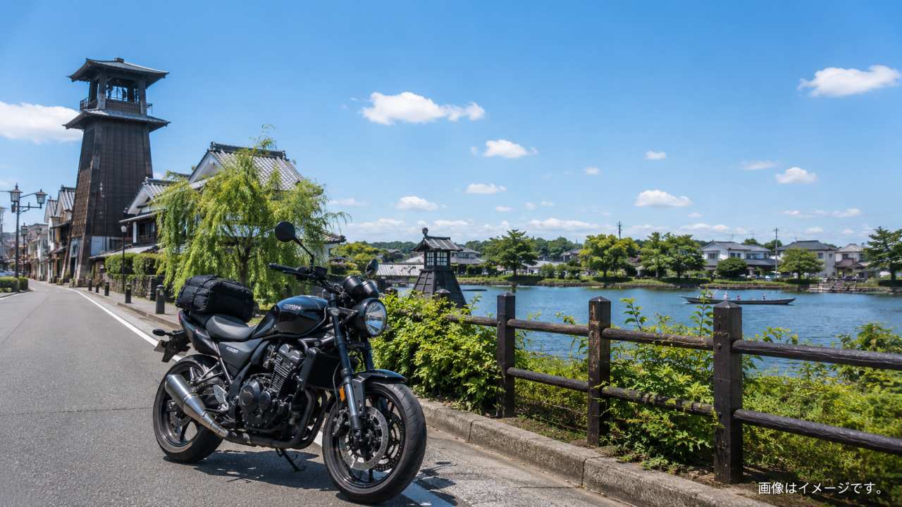 埼玉県の郊外道路を走るツーリング風景、前景に停車したバイク、背景に川越の町並みや湖畔を連想させる自然、晴れた休日の爽やかな雰囲気