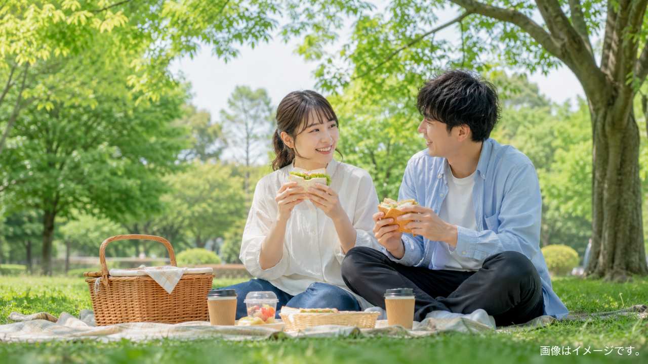 カップルが埼玉の緑豊かな公園でサンドイッチと飲み物を楽しむ落ち着いたピクニック風景