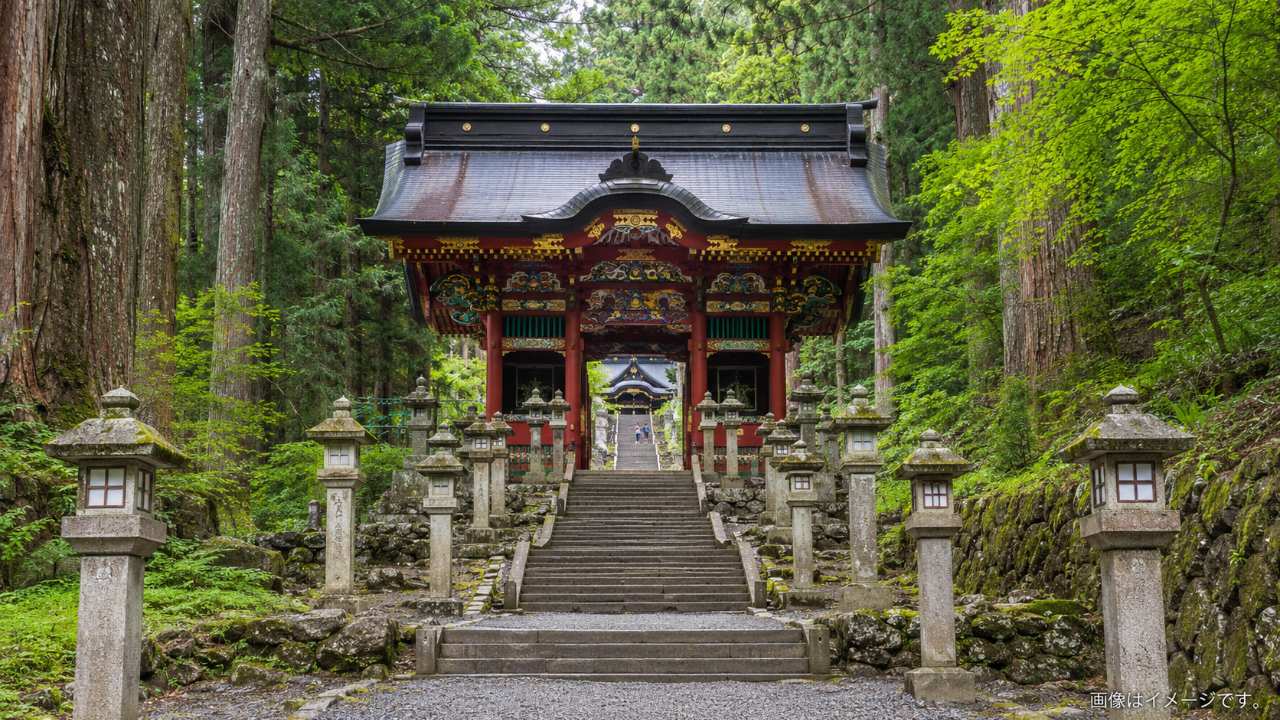 三峯神社の参道にある石段、石灯籠、鮮やかな随身門を写した実写風の写真。駐車場から拝殿まで歩く際の坂道や階段が分かる構図