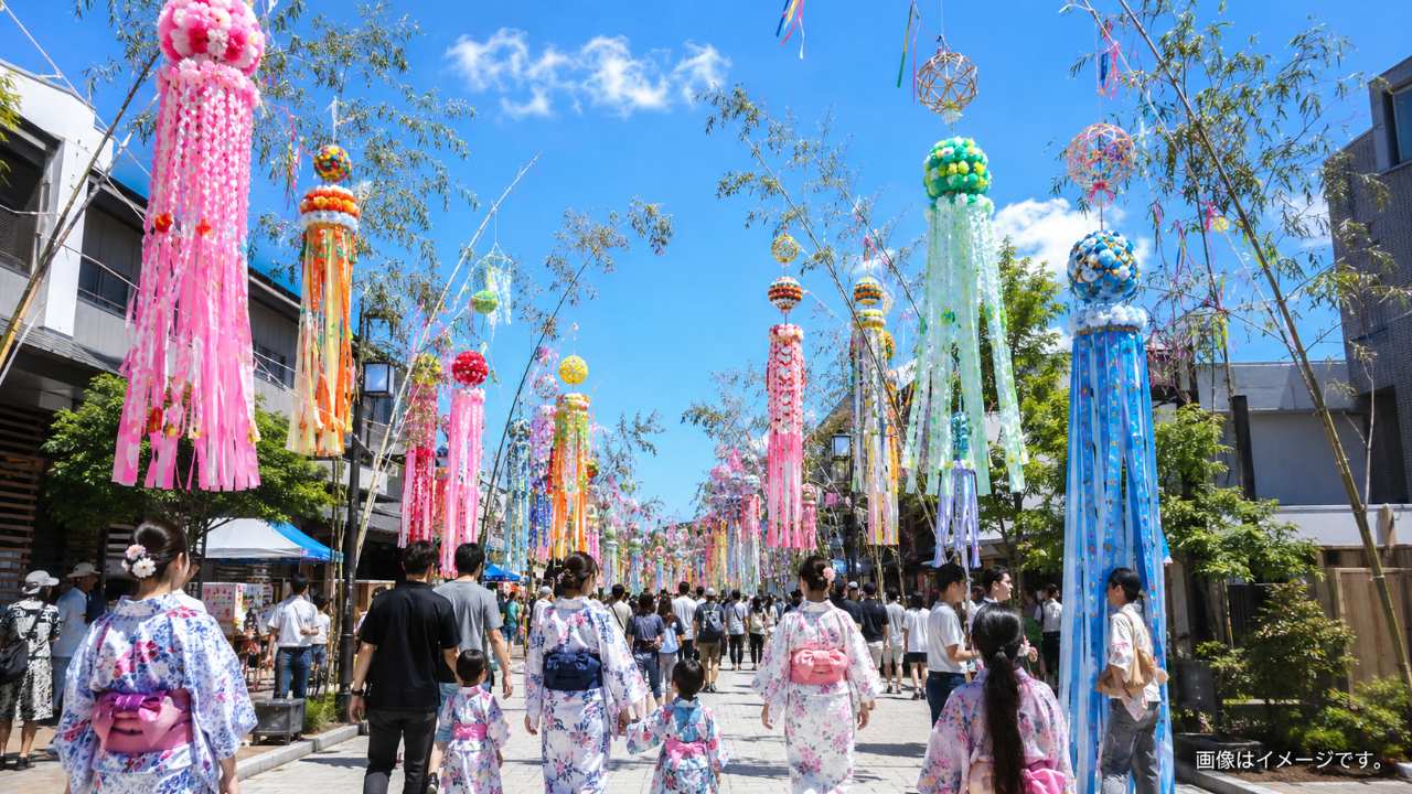埼玉県狭山市の夏祭りをイメージした写真風のアイキャッチ画像。青空の下、商店街の通りに色鮮やかな大型の七夕竹飾りと長い吹き流し